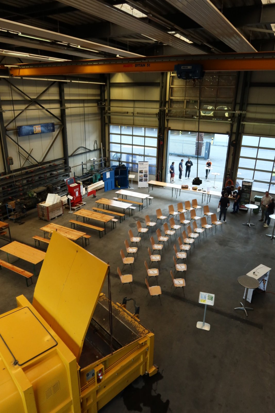 TeilnehmVogelperspektive der Werkhalle bei GETAG mit aufgestellten Stuhlreihen, Festbänken und Maschinen für den Sicherheitsworkshop.ende und Kursleiter des GETAG-Workshops während der Praxiseinheit in der Werkstatthalle an einer Werkbank.